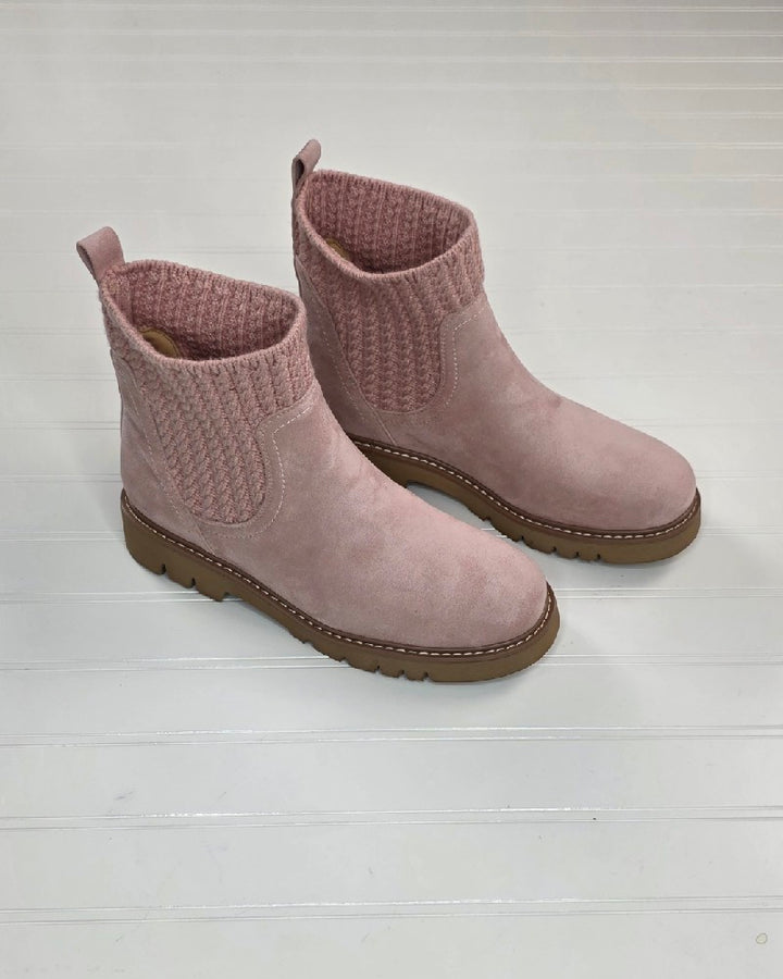 A pair of Corkys Keep Me Warm Boot by Corkys in pink, with a cable knit upper and a cozy suede-like finish, are elegantly displayed on a white wooden surface.