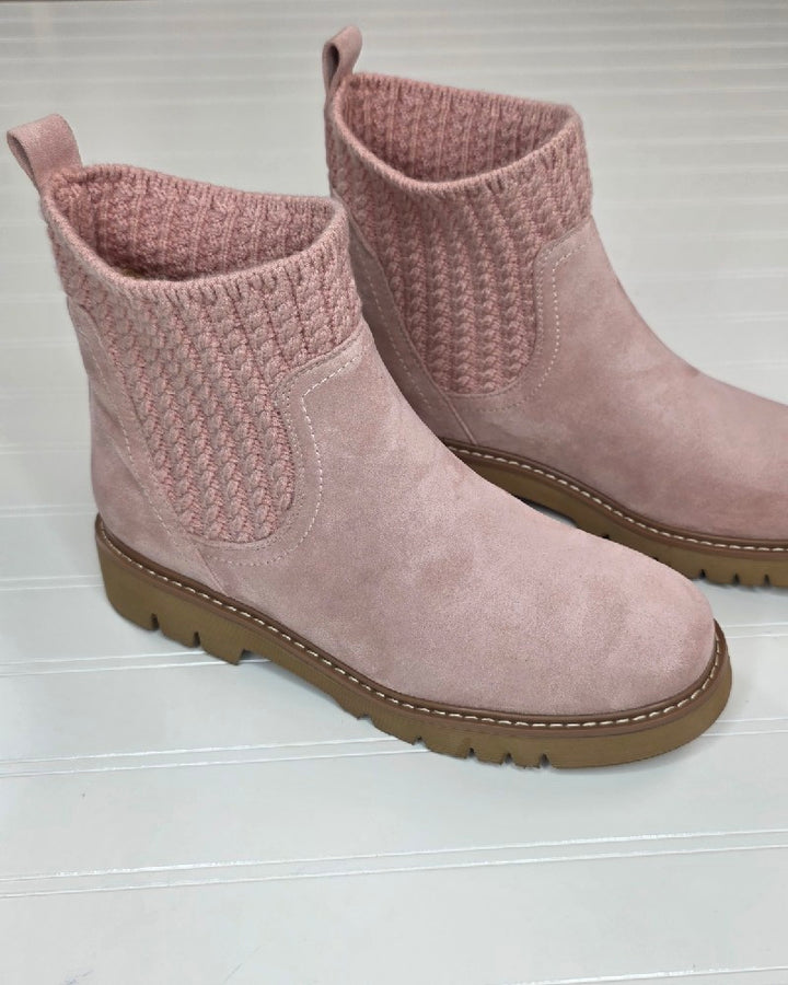 A pair of pink Keep Me Warm Boots by Corkys, featuring a cozy cable knit upper around the ankle and brown rubber soles, is displayed on a light-colored, ridged surface.