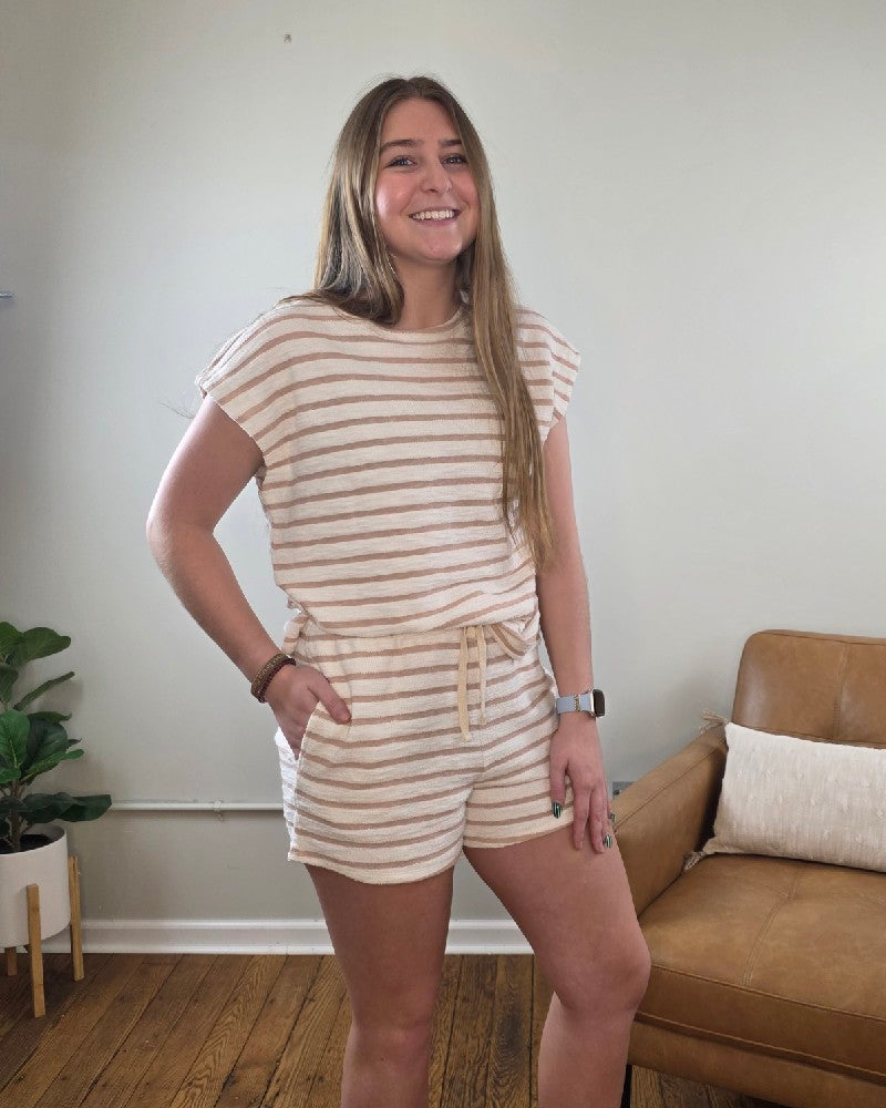 A woman smiles as she poses in the London Striped Short Sleeve Top and Shorts Set by HYFVE, Inc. She stands before a light gray wall and tan leather chair, highlighting her casual cotton outfit.