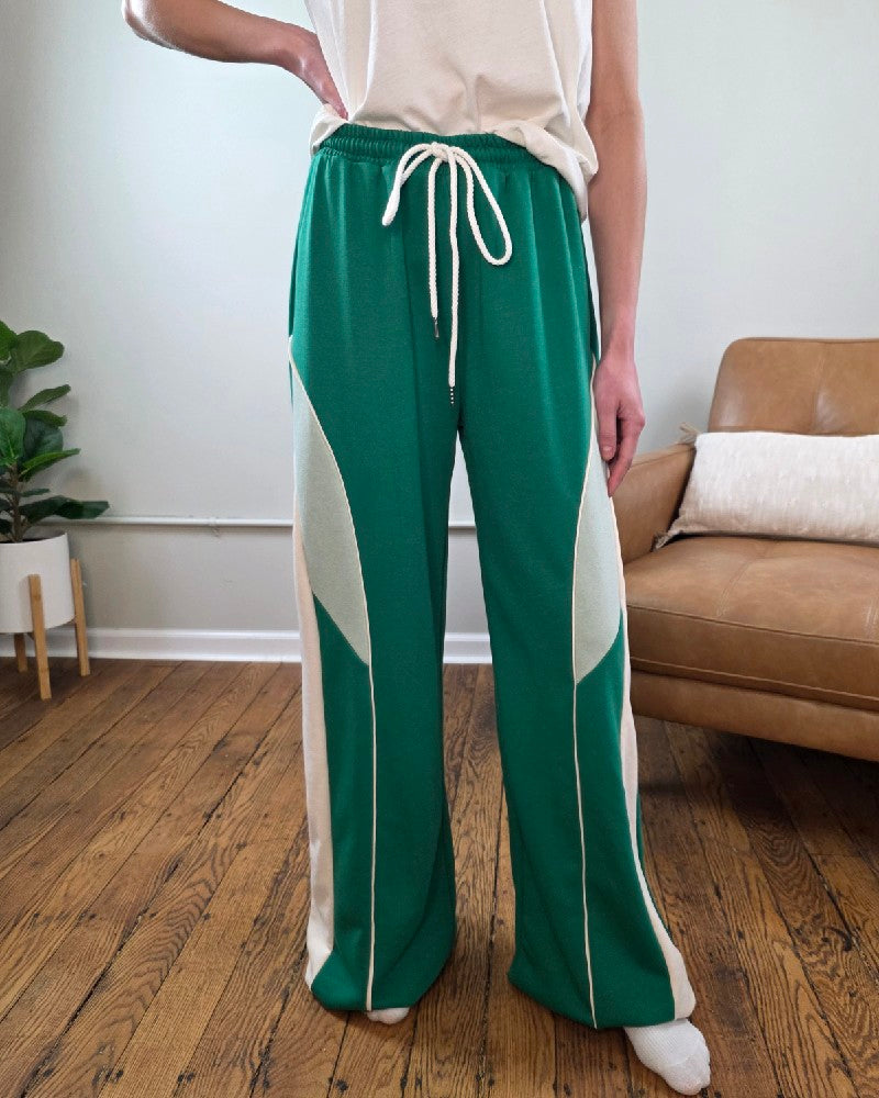 Person wearing the Trinity Wide Leg Lounge pants in green and white with a white top in a room with a couch and plant.