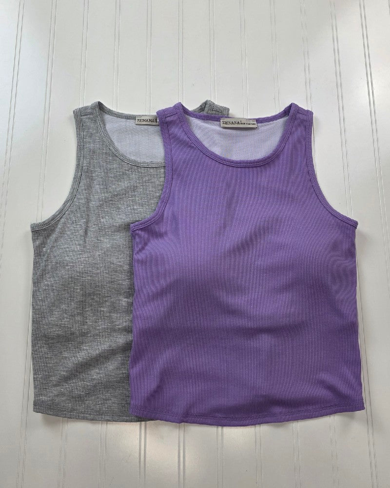 Two ZENANA Vicky Ribbed Racer Back Tanks with built-in bras, one light gray and one purple, are laid flat on a white wood surface. The purple tank is placed in front of the gray, showcasing the minimalist racer back design.