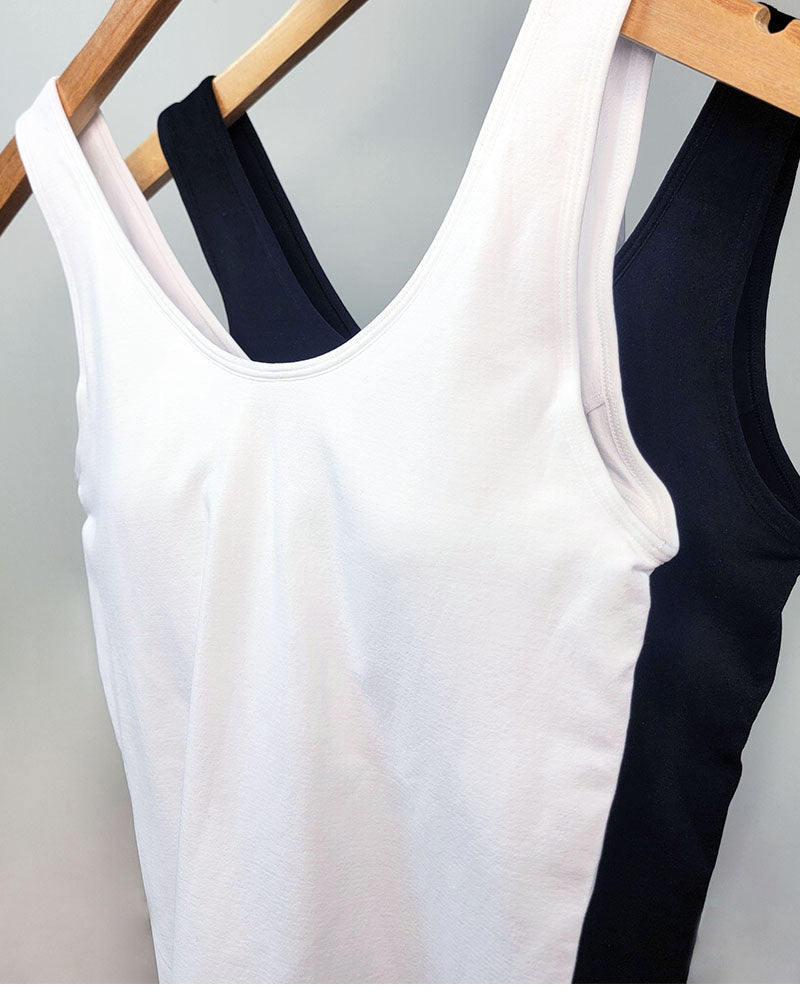 Two Yelete Group Wide Strap Layering Tanks with Built-in Bra, one in white and one in black, hang on wooden hangers against a plain background.