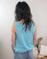 A person with long hair stands in front of a couch, wearing the Ayla Ribbed Tank by Cosmos + Clover Boutique.