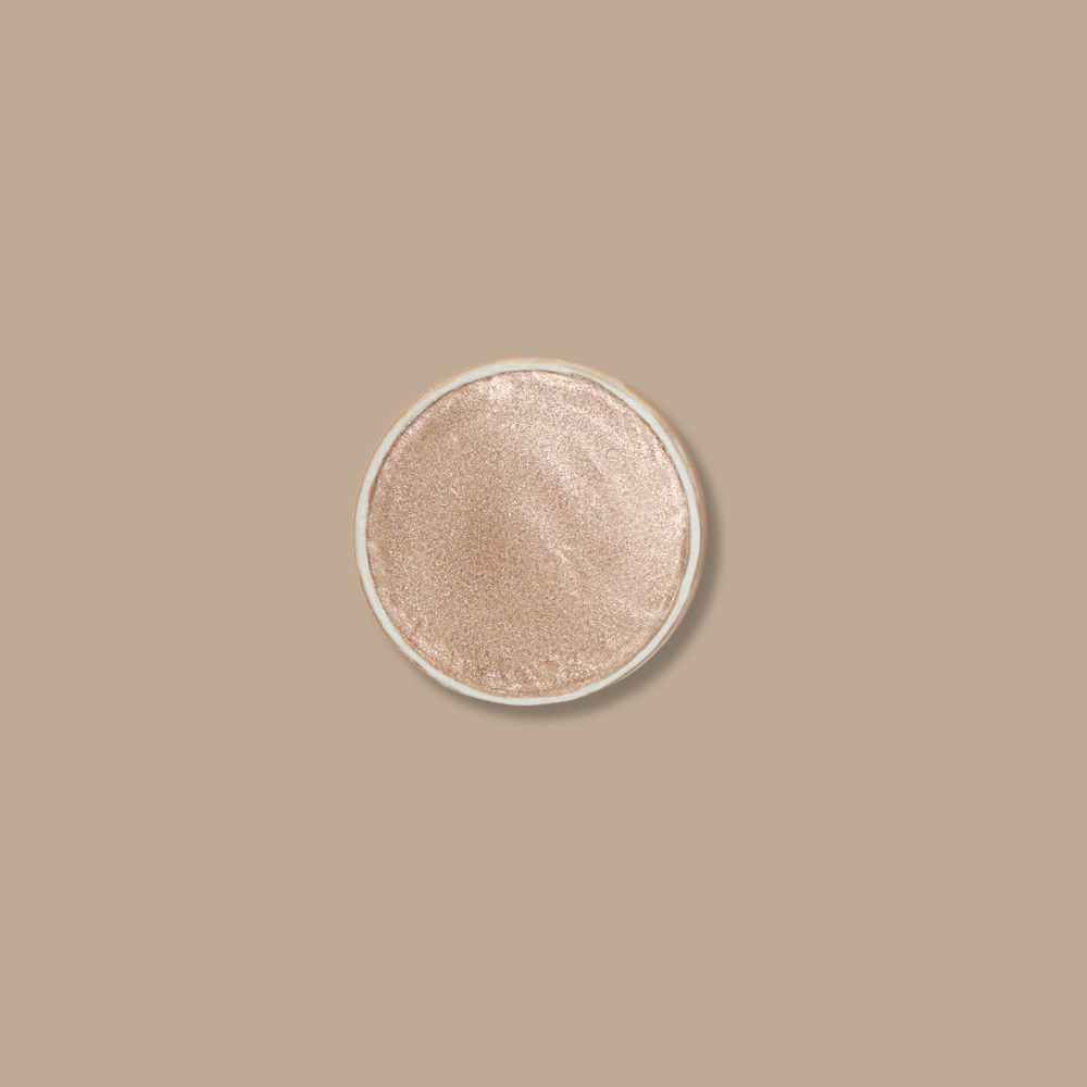The Minori Zero Waste Cream Highlighter Mini in Champagne, with a smooth metallic finish, sits centered on a matching beige background. This clean beauty essential delivers a radiant, effortless glow.