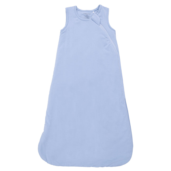 The Angel Dear Solid Blue Fog Sleep Bag is a sleeveless, light blue bamboo sack with a rounded bottom, subtle texture, and a fabric knot near the neckline, displayed against a white background.