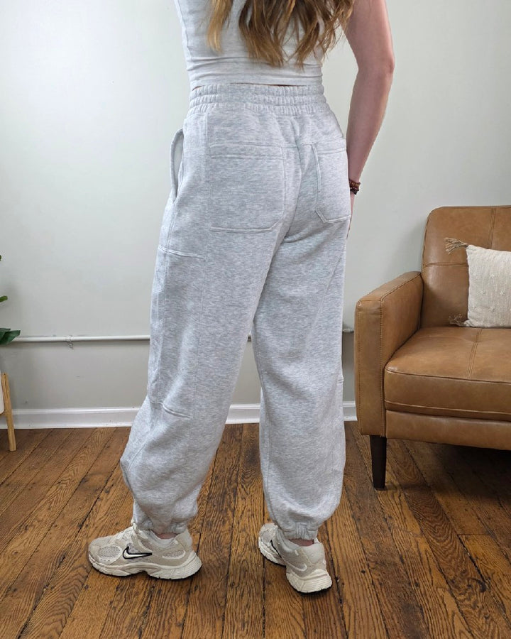 A person wearing heather grey Amy Grey Joggers by Rae Mode, featuring an elastic waistband and cuffs, paired with athletic sneakers.