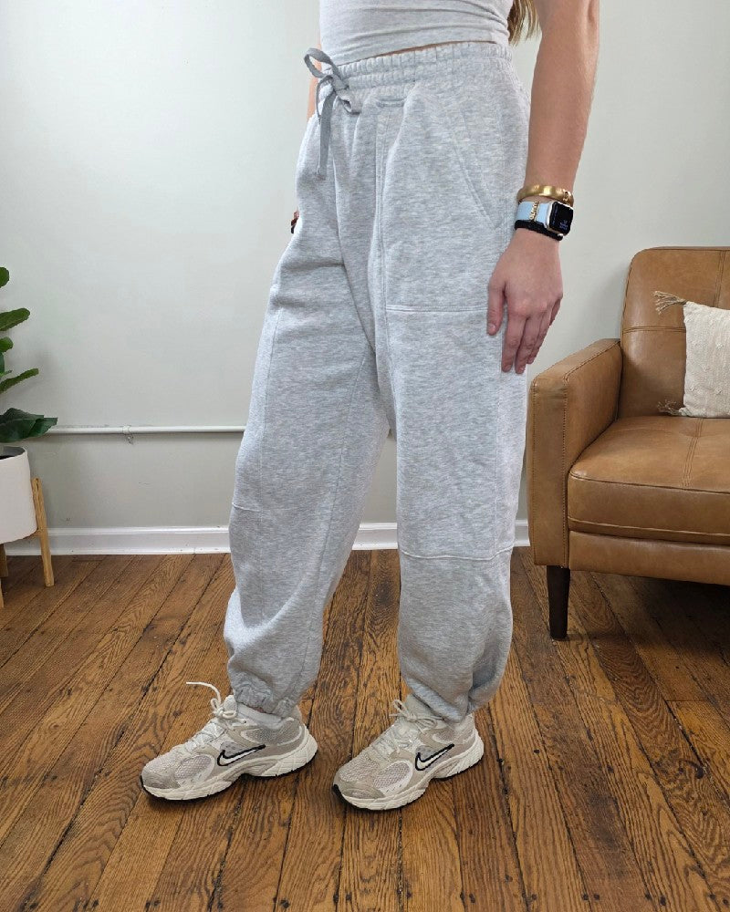 Amy Grey Joggers in heather grey with an elastic drawstring waist and cuffed ankles, paired with off-white athletic sneakers.