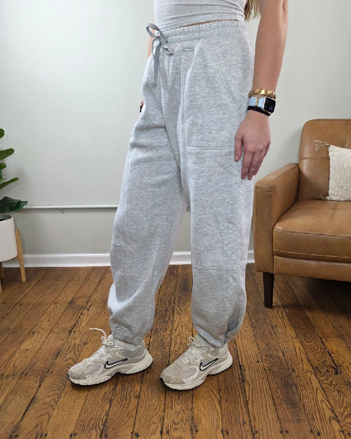 Amy Grey Joggers in heather grey with an elastic drawstring waist and cuffed ankles, paired with off-white athletic sneakers.