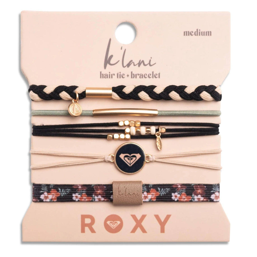 A set of five K’lani hair tie bracelets from the “Roxy Coastal Drift” collection features black, beige, and floral-patterned braided bands with unique charms and metal accents, all displayed on a medium card for a beach-inspired accessory look.