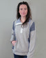 A woman with long brown hair wears the Hem & Thread Shay Striped Mix Pullover in light gray and white, standing against a plain gray wall. She looks slightly right with a neutral expression, one hand casually in her pocket.