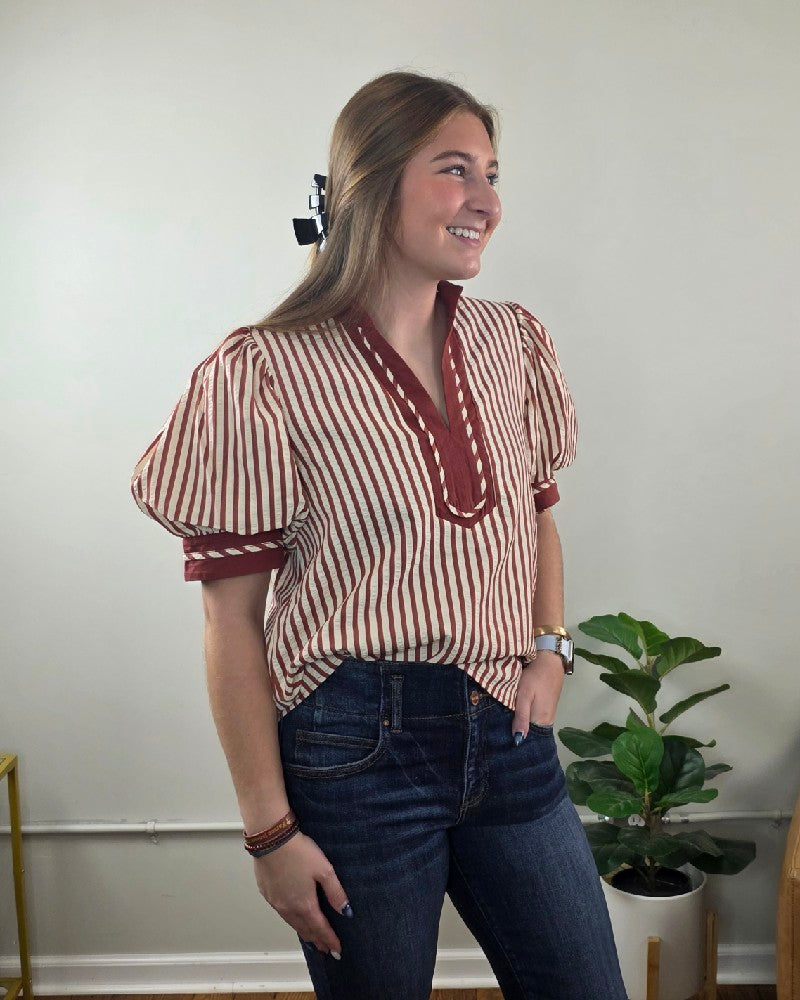A person wears a rust striped Brittany V neck Puff Sleeve Stripe Blouse with a V-neck and puff sleeves, paired with dark blue jeans.