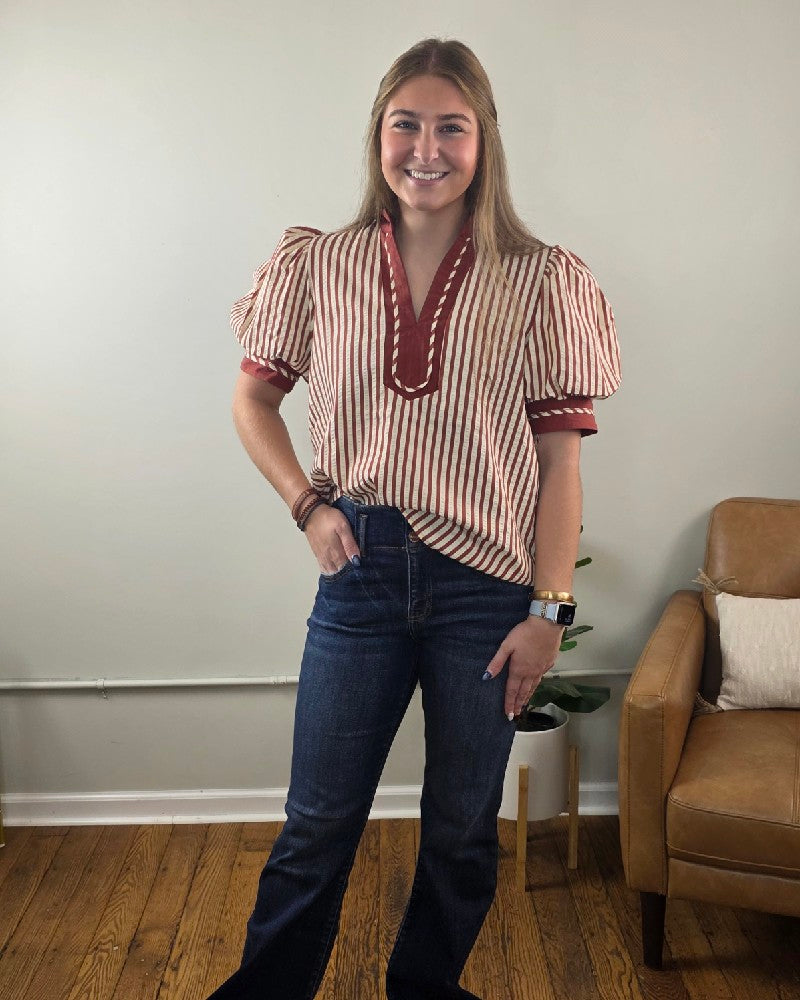 A woman wearing a rust striped Brittany V neck Puff Sleeve Stripe Blouse with a V-neck and short puff sleeves, paired with dark wash jeans.