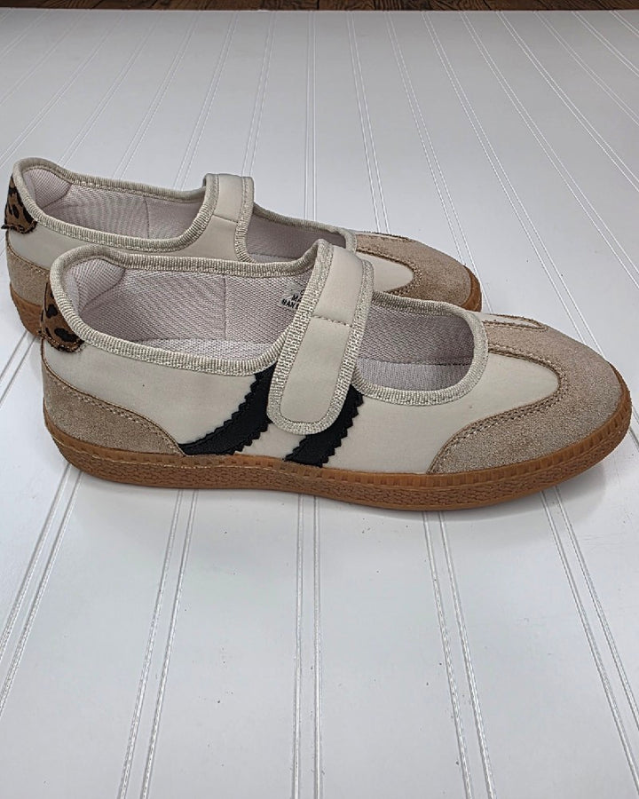 Introducing the Calm Down Sand Combo Slip on Shoe by Corkys—a pair of beige Mary Jane sneakers featuring brown suede accents, black wavy stripes along the sides, and durable gum soles. These neutral sneakers are shown resting on a white textured surface.