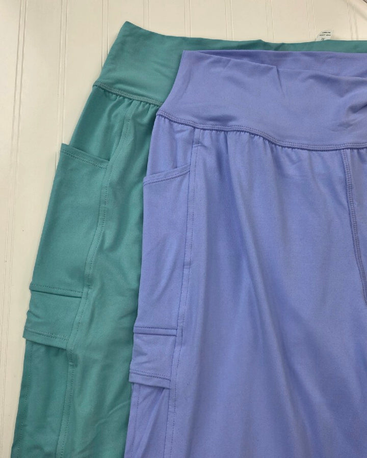 Two pairs of buttery soft high-waisted Carolina Joggers by Rae Mode with side cargo pockets in teal and lavender.