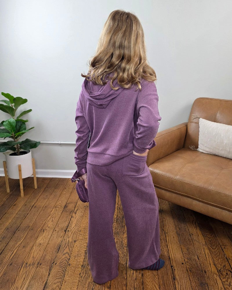 A girl seen from the back wearing a purple Ellen Tween Girls Snap Hoodie, Wide Leg Pants and Wristlet Set by 90 Degree by Reflex, holding a matching small purple wristlet.
