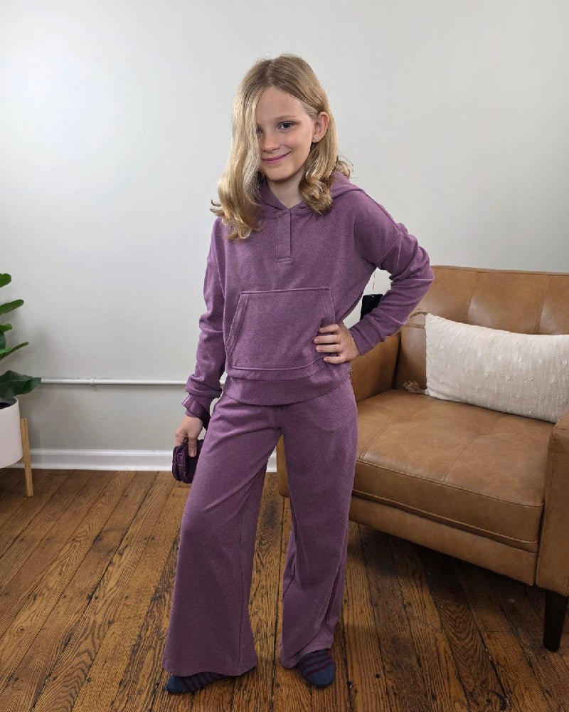 A girl wearing a purple 90 Degree by Reflex Ellen Tween Girls Snap Hoodie, Wide Leg Pants and Wristlet Set, holding the included small wristlet.