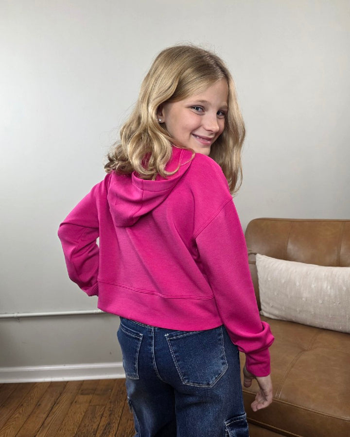 A young girl smiles over her shoulder while wearing a bright pink 90 Degree by Reflex Erin Tween Girls Cutout Scuba Hoodie, which features a cutout on the back.