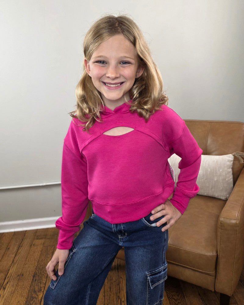 A young girl wears a bright pink Erin Tween Girls Cutout Scuba Hoodie with a cutout neckline paired with blue jeans.