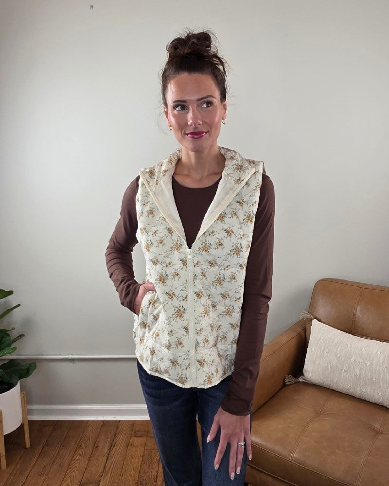 A woman wears a cream-colored, lightweight Staccato Isla Floral Printed Zip Up Vest over a long-sleeved brown shirt.
