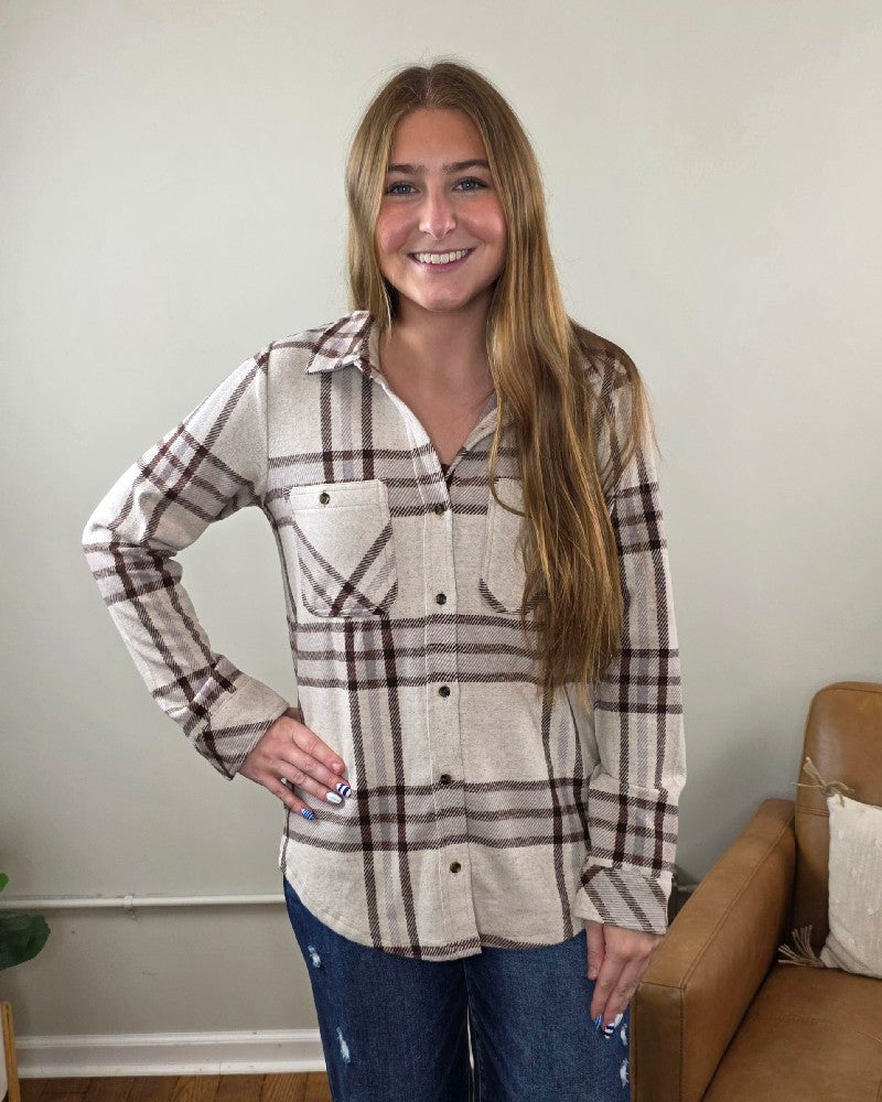 A young woman with long light brown hair is wearing the Thread &amp; Supply Lewis Plaid Button Down Flannel in cream and brown, paired with blue jeans. She stands indoors with one hand on her hip, smiling at the camera.