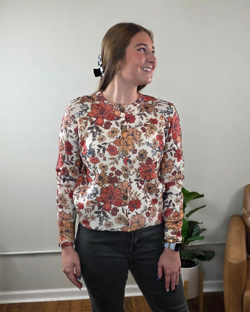 A person wearing a LovLov Megan Vintage Wildflower Cardigan with a cream base and a red, orange, and brown button-down floral print.