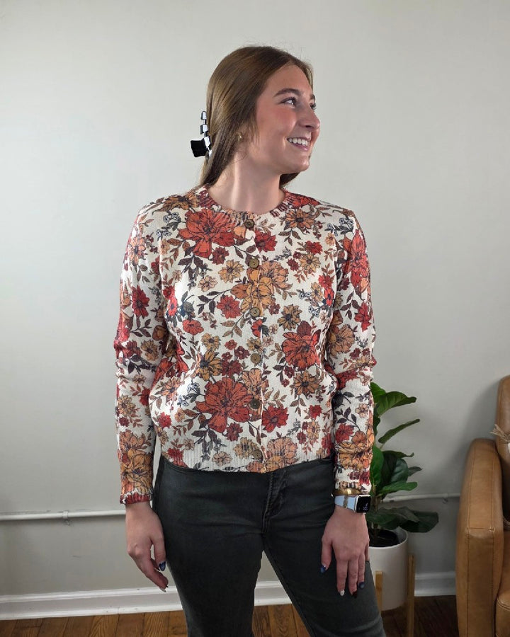 A person wearing a LovLov Megan Vintage Wildflower Cardigan with a cream base and a red, orange, and brown button-down floral print.
