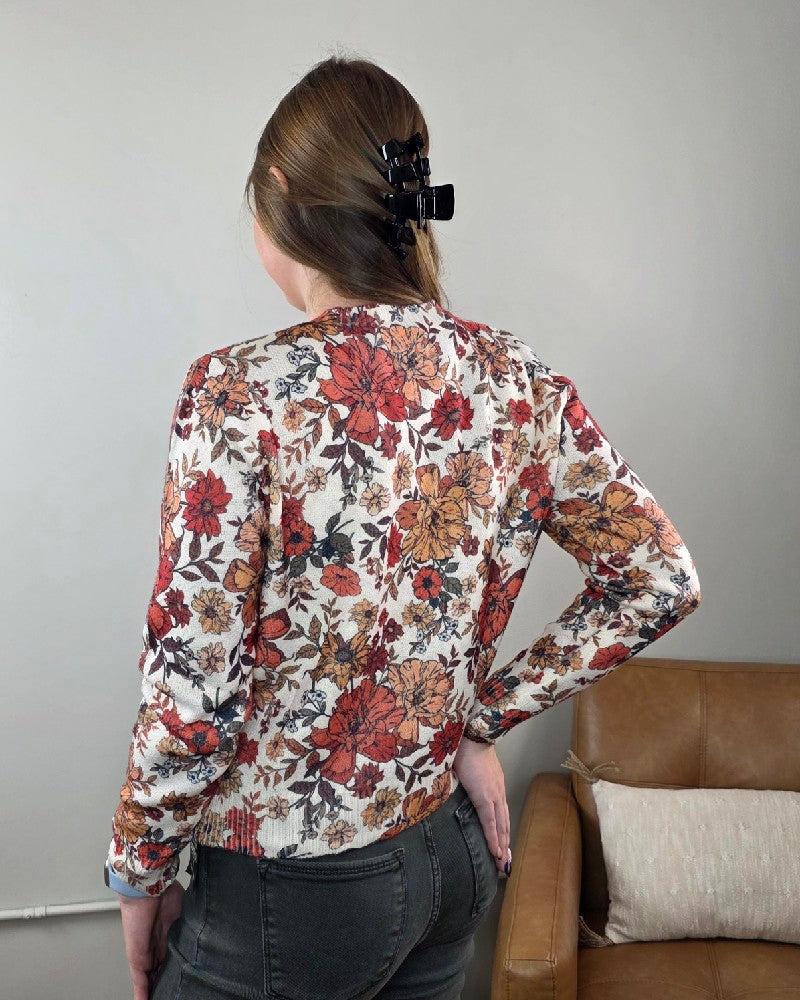 A person seen from behind wearing the cream-colored Megan Vintage Wildflower Cardigan by LovLov, featuring a red and orange floral pattern.