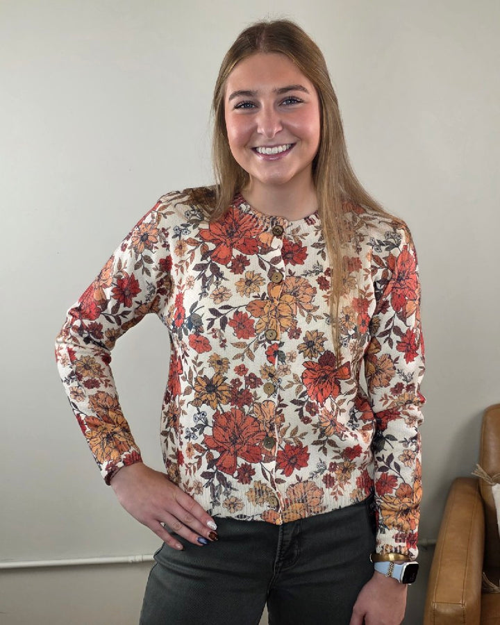 A woman wearing a cream-colored Megan Vintage Wildflower Cardigan with an orange and brown wildflower pattern.