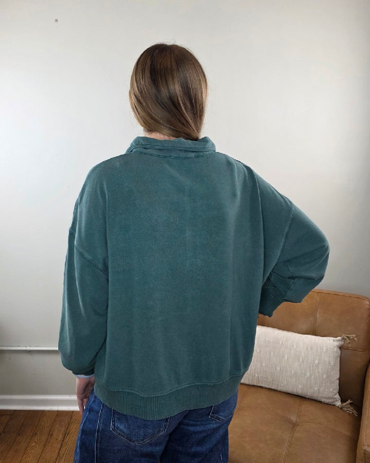 Back view of a person wearing a dark green, relaxed fit Nora Button Front Sweatshirt and blue jeans.