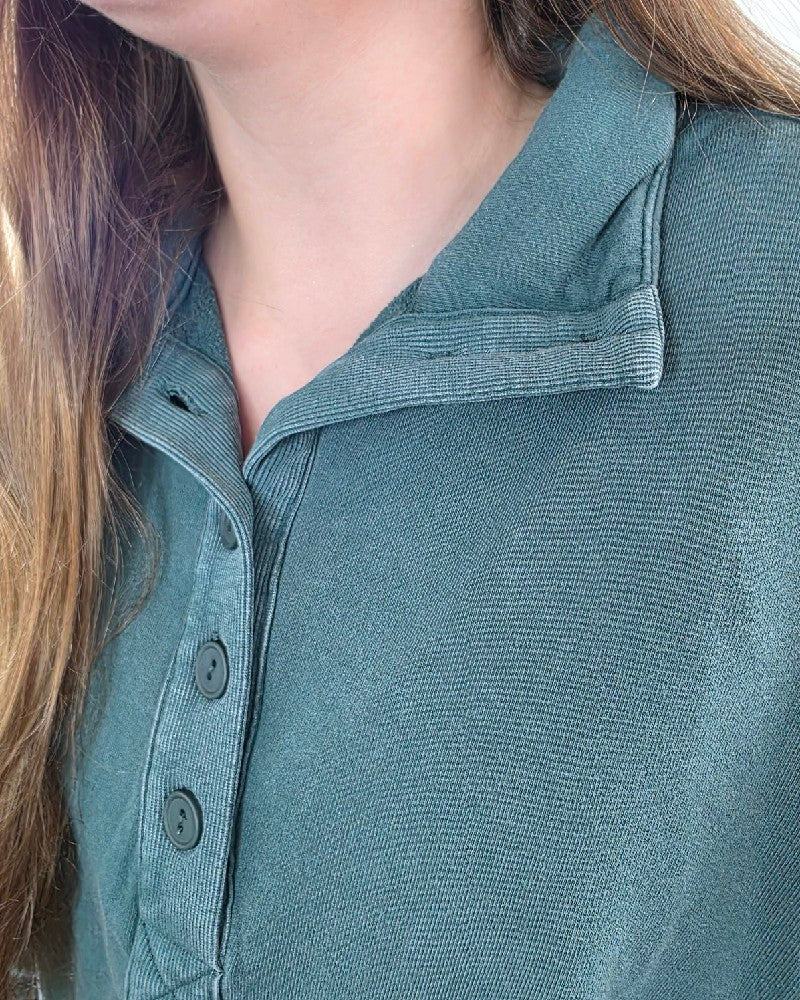A close-up of a person wearing a dark green, relaxed fit Nora Button Front Sweatshirt with a collared, long-sleeve design and a button-front placket.