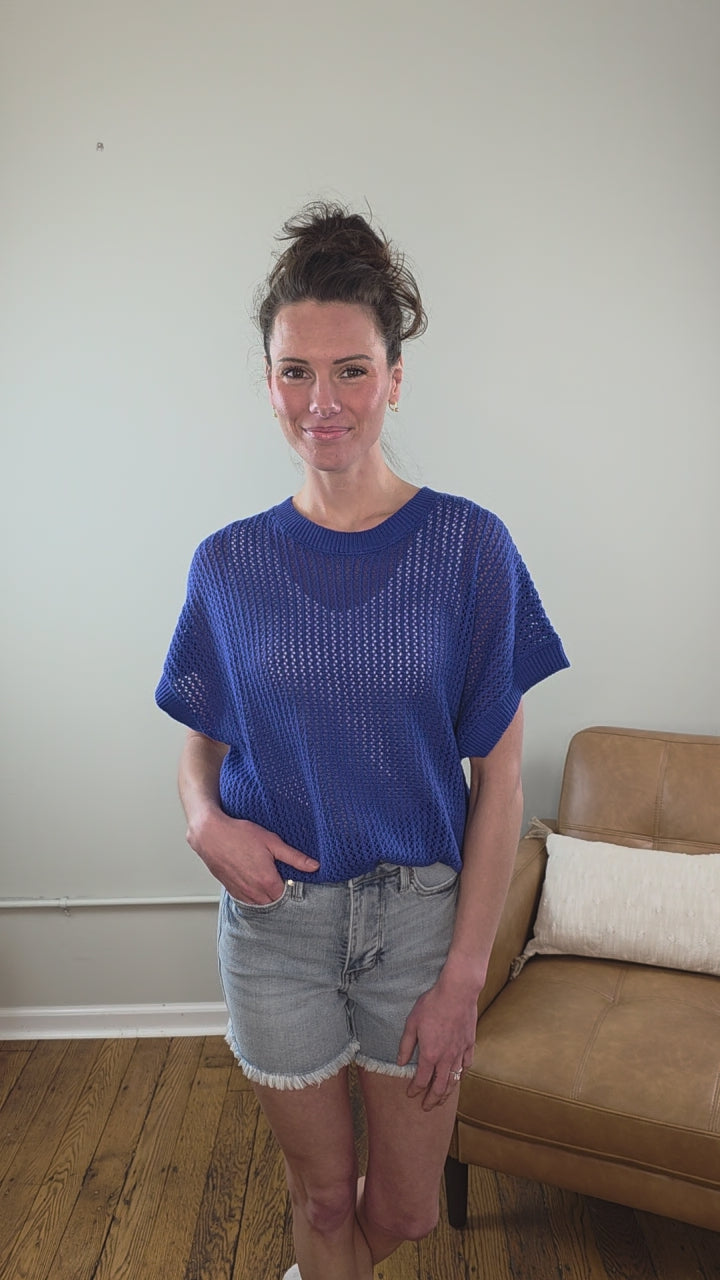Woman wearing the Camille Open Knit Short sleeve Top a blue with denim shorts indoors.