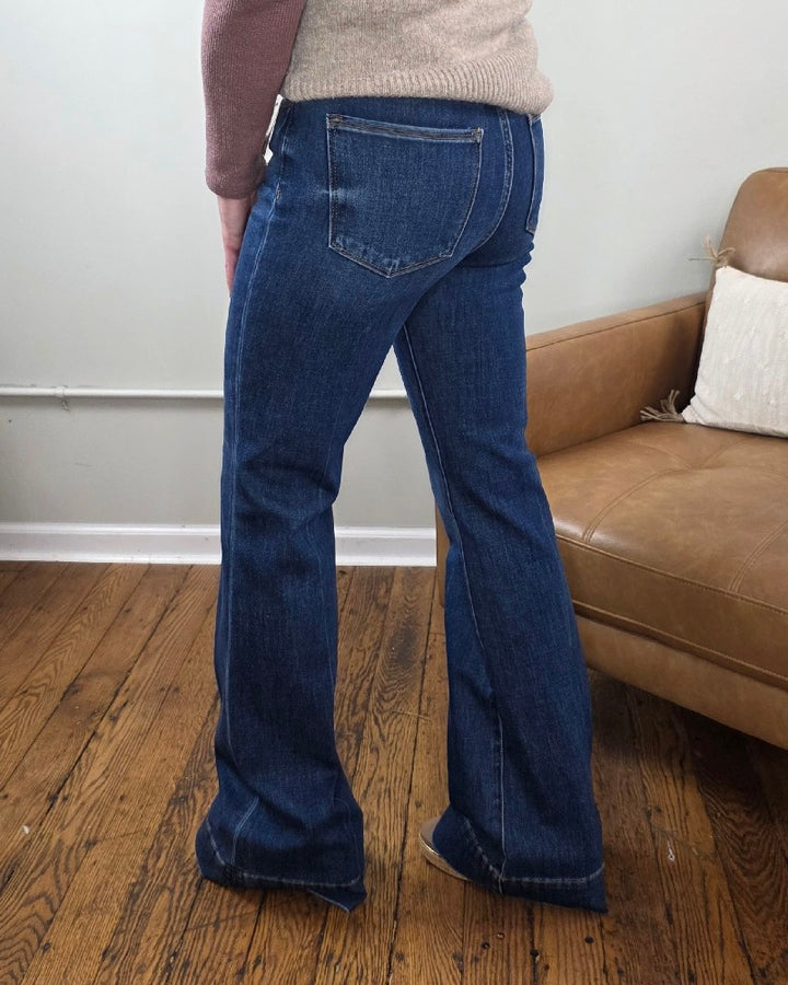 A person wearing the Rachel High Rise Trouser Flares with Tummy Control from Risen stands on a wooden floor near a tan leather couch with a white pillow.