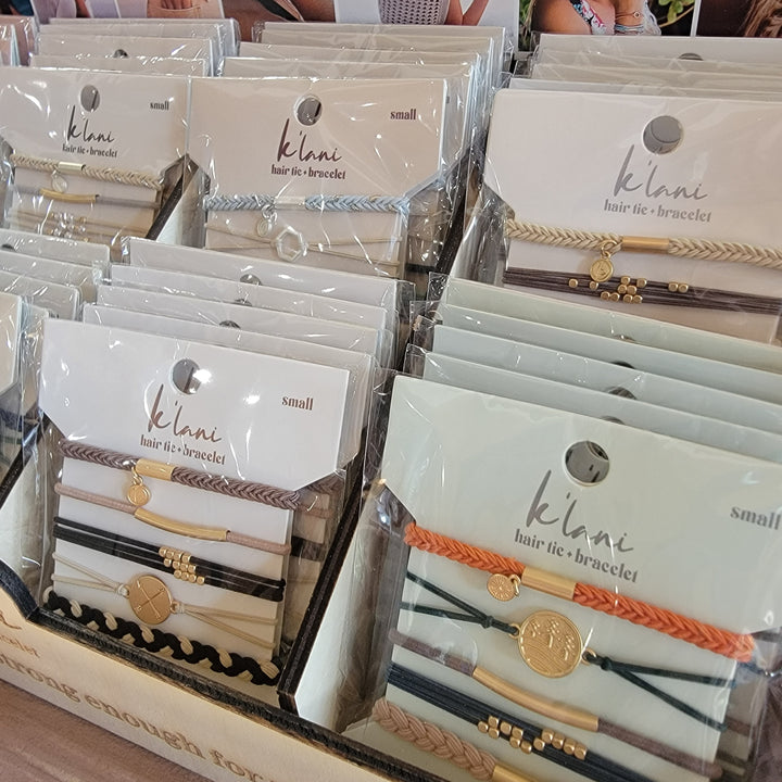 K'lani Wholesale’s K'lani Hair Tie Bracelet Sets are neatly displayed in assorted trendy colors and designs, each set packaged in clear plastic with a white label and gold accents.