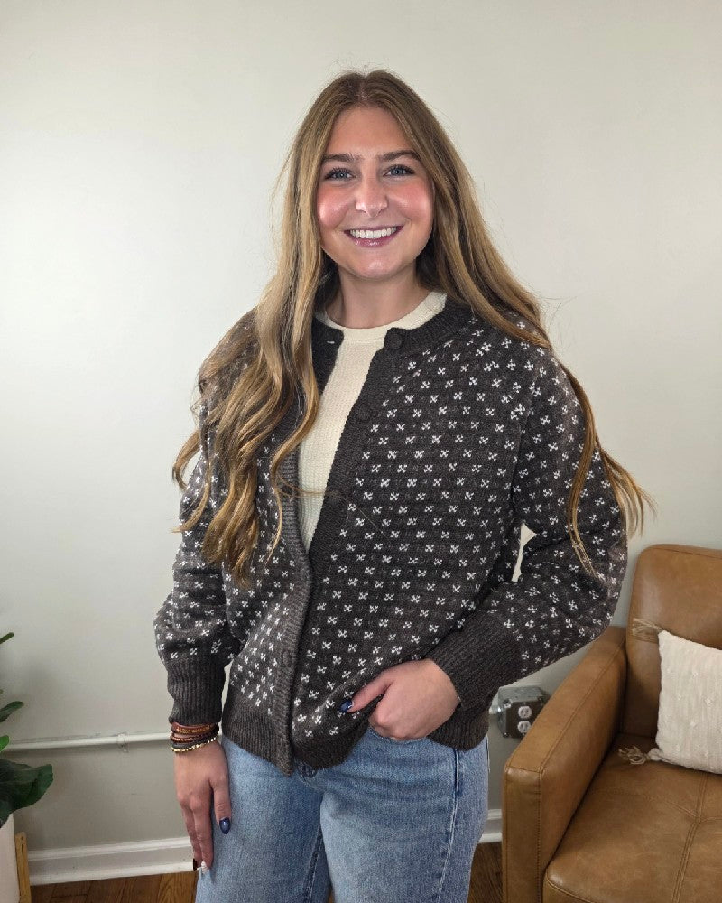 A smiling woman wears a Staccato Sylvia Detailed Button Down Sweater in chocolate brown with a repeating white floral pattern over a cream-colored top.