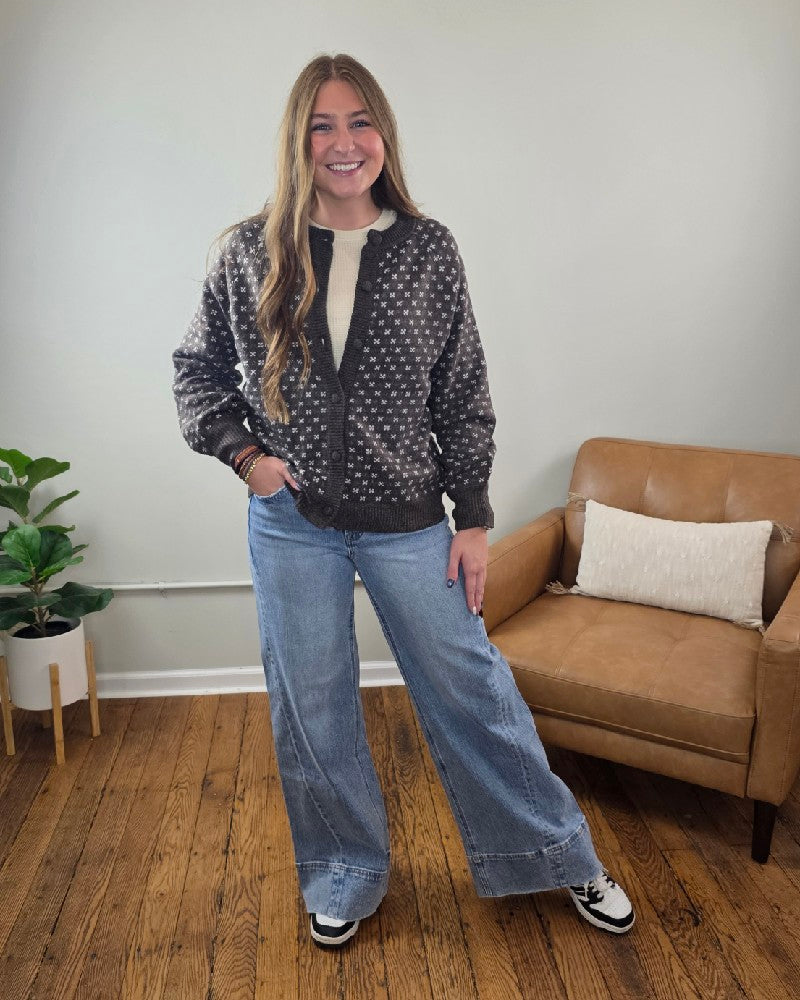 A woman wearing a chocolate brown vintage Staccato Sylvia Detailed Button Down Sweater with a small geometric pattern over a cream shirt, paired with wide-leg blue jeans.