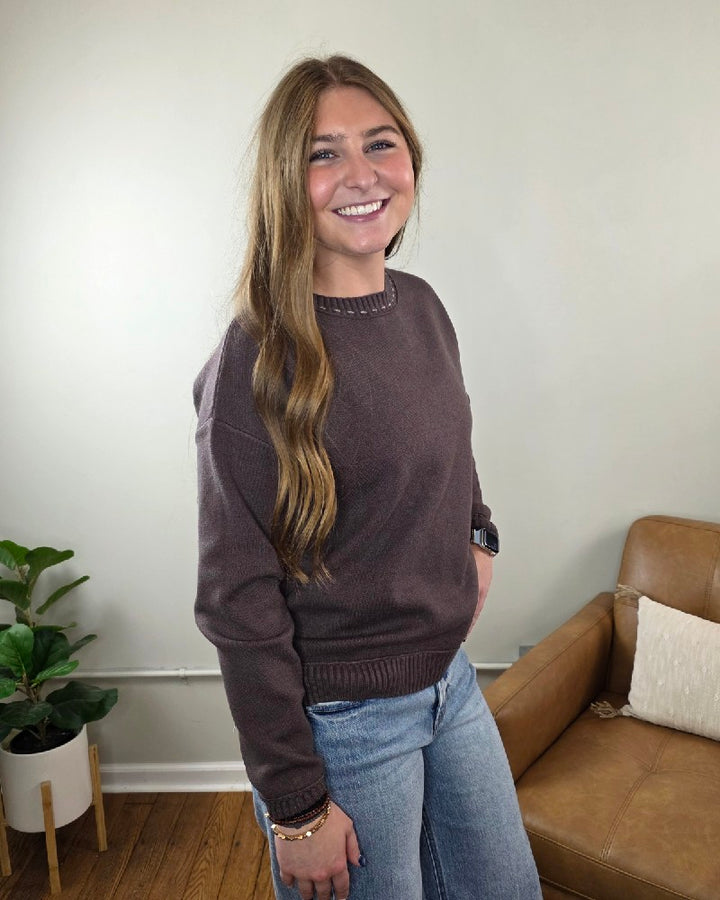 A woman wearing a cozy, brown long-sleeved Staccato Willow Stitch Detailed Sweater and blue jeans.