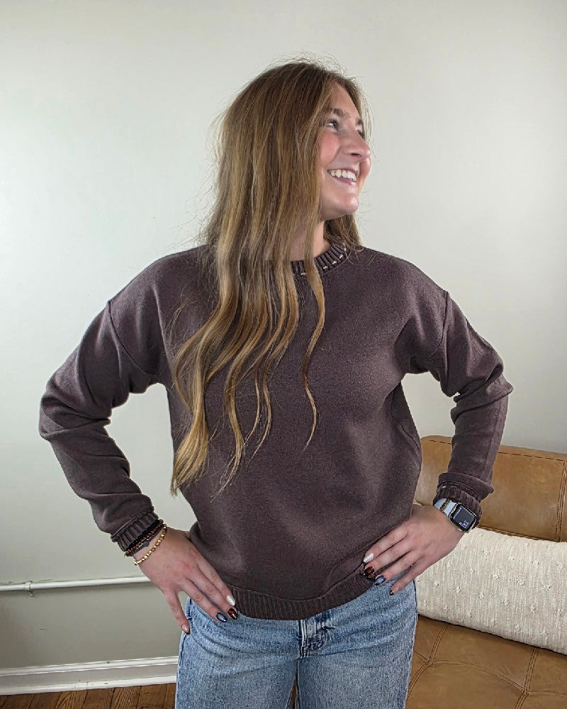 A person wears a cozy brown long-sleeved Staccato Willow Stitch Detailed Sweater with stitch detailing at the crew neckline and cuffs.