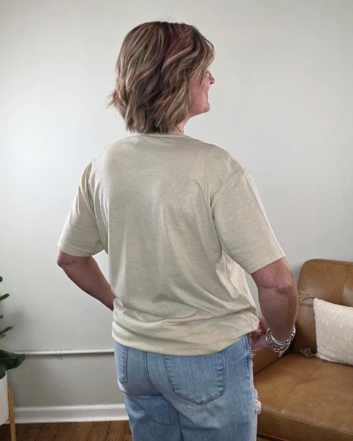A person wearing a cream-colored Witch Graphic Tee and blue denim jeans.