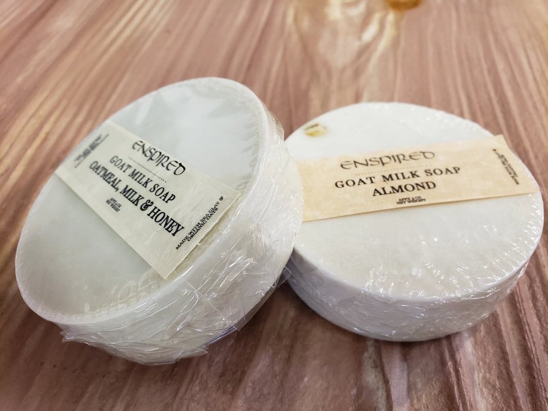 Two Enspired Handmade Soap bars, one Oatmeal Milk & Honey and the other Almond, wrapped in plastic, are placed on a wooden surface displaying the Enspired brand.