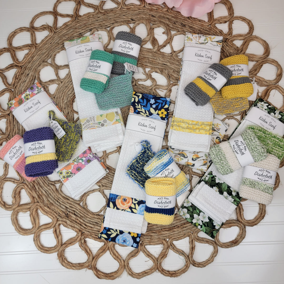 Colorful Nanny K's Dishcloths by Nanny K's Kitchen Kreations, some featuring floral patterns, are neatly packaged in matching sets and displayed on a woven placemat atop a white surface.