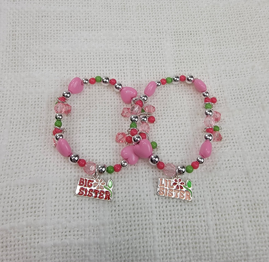 Two beaded bracelets with pink, green, and silver beads from 2HOPE Accessories, Inc. Each bracelet has a "Big Sister" or "Lil Sister" charm—ideal to pair with Girls Charm Jewelry: Big Sister/Little Sister Sets.
