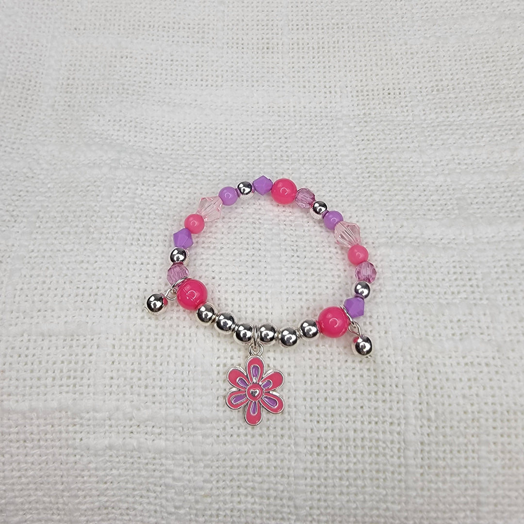 The Girls Charm Jewelry: Bracelets by 2HOPE Accessories, Inc features pink, purple, and silver beads with a dangling pink flower charm, displayed on white textured fabric—ideal for girls' jewelry collections.