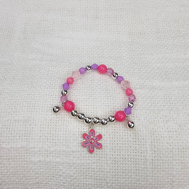 The Girls Charm Jewelry: Bracelets by 2HOPE Accessories, Inc features pink, purple, and silver beads with a dangling pink flower charm, displayed on white textured fabric—ideal for girls' jewelry collections.